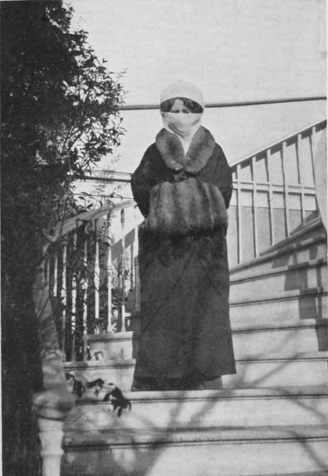 The author is shown standing on an outside staircase facing the camera with her hair mostly covered, the yashmak veil covering all of her face below the eyes. She is wearing a long flowing robe with a fur-like collar, and her hands are covered by a fur-like muff.